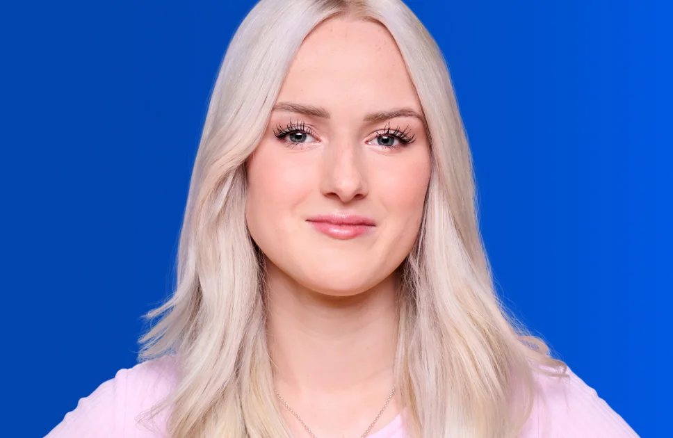 Junge Frau mit langen hellblonden Haaren vor kräftig blauem Hintergrund.