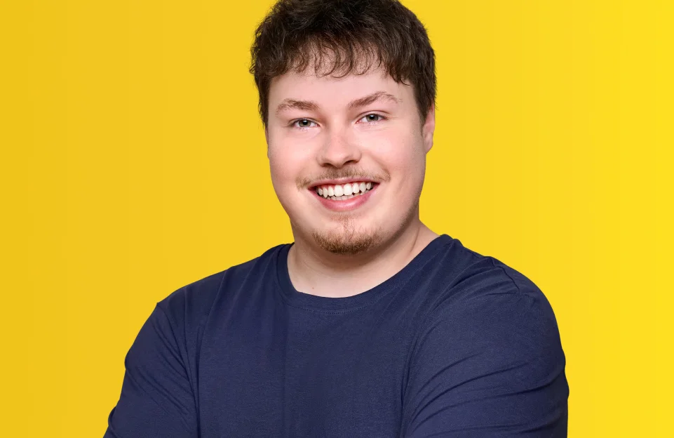 Lächelnder junger Mann im dunkelblauen T-Shirt vor gelbem Hintergrund.